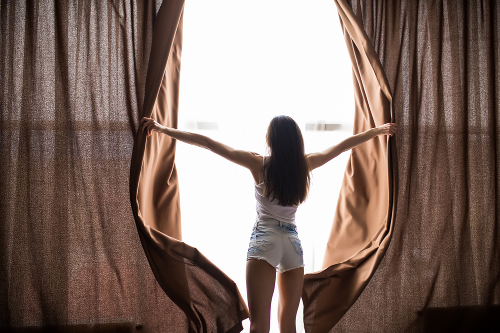 窓のカーテンをあける女